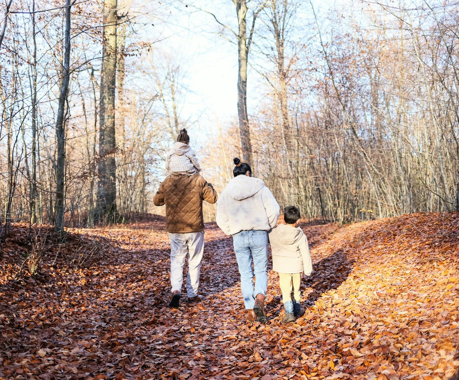 A family walking a leaf-covered path through autumn woods
